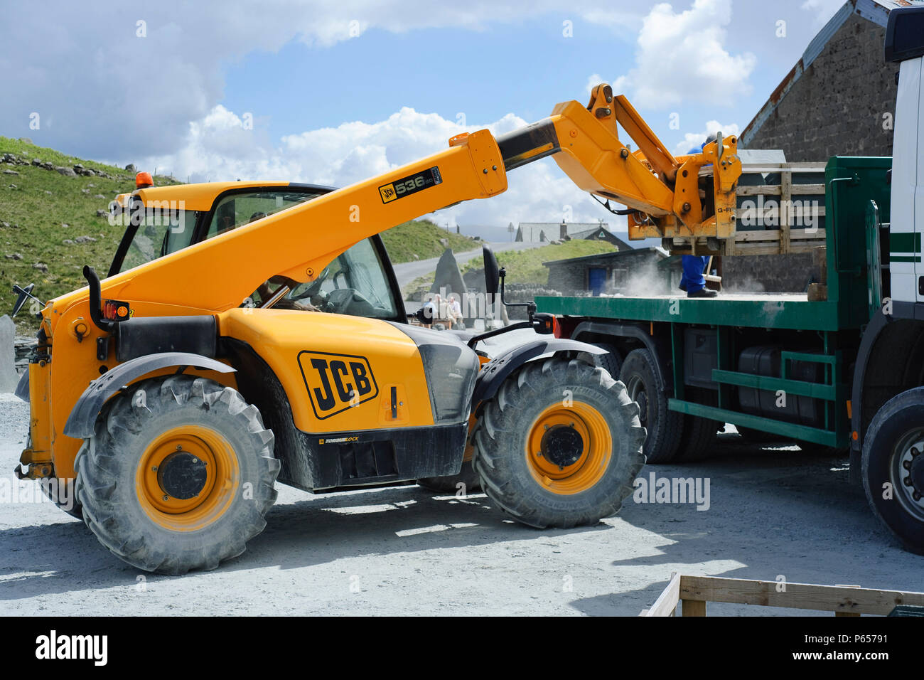 JCB telescopic forklift lifting materials from flat bed truck Stock Photo