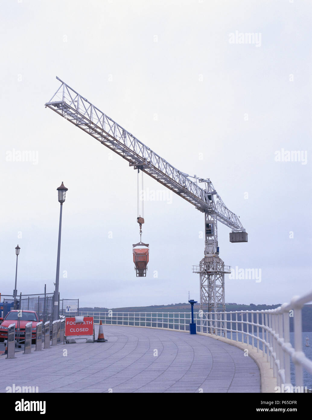 Tower crane lifting concrete hopper over closed footway. Renovation of