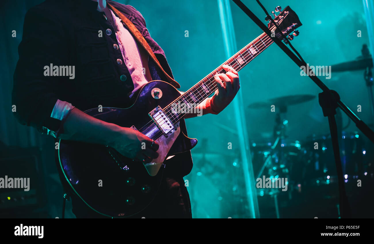 Guitarist on stage plays solo on electric guitar in cyan lights Stock Photo