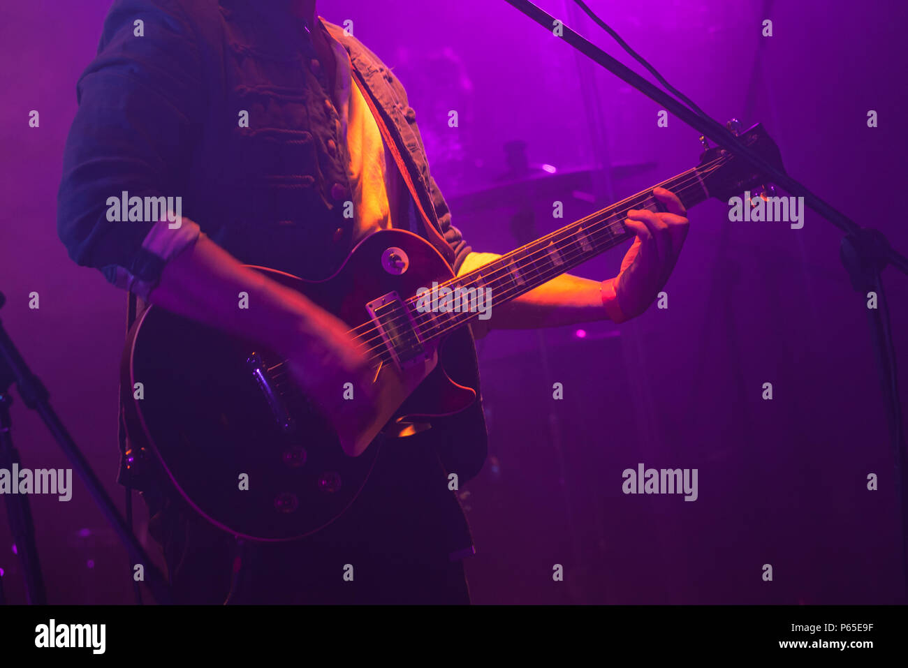 Guitarist plays on electric guitar in purple scenic illumination, soft selective focus Stock Photo