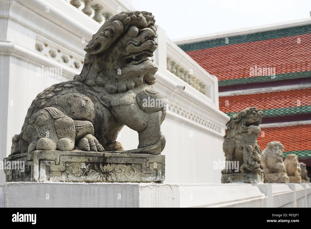 A row of ancient carved stone lions and other statues stand guard on the grounds of the Royal Palace in Bangkok, Thailand on a sunny day Stock Photo