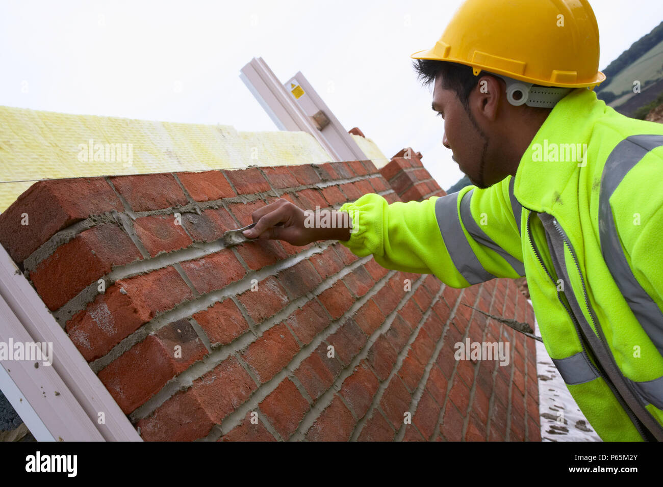 Bricklayer smoothing mortar on a newly erected brickwall. House building site, England, UK. Stock Photo