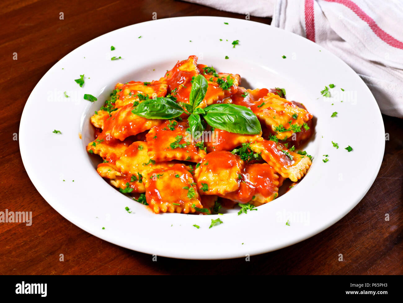 Fresh ravioli pasta with basil leaf and tomato sauce on a white plate. Stock Photo