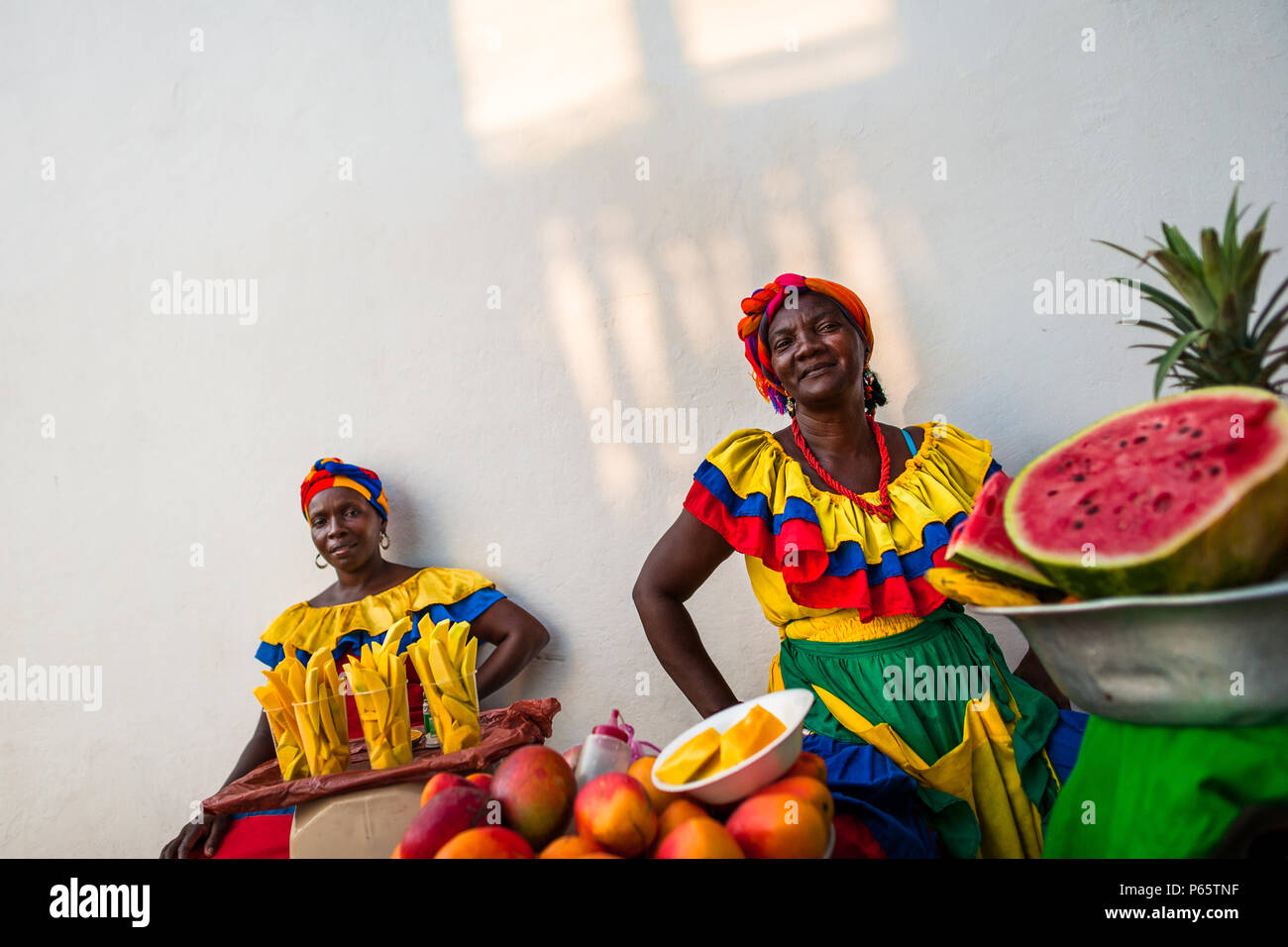 Afro-Colombian women, dressed in the traditional ‘palenquera’ costume, sell fruits on the street of Cartagena, Colombia. Stock Photo
