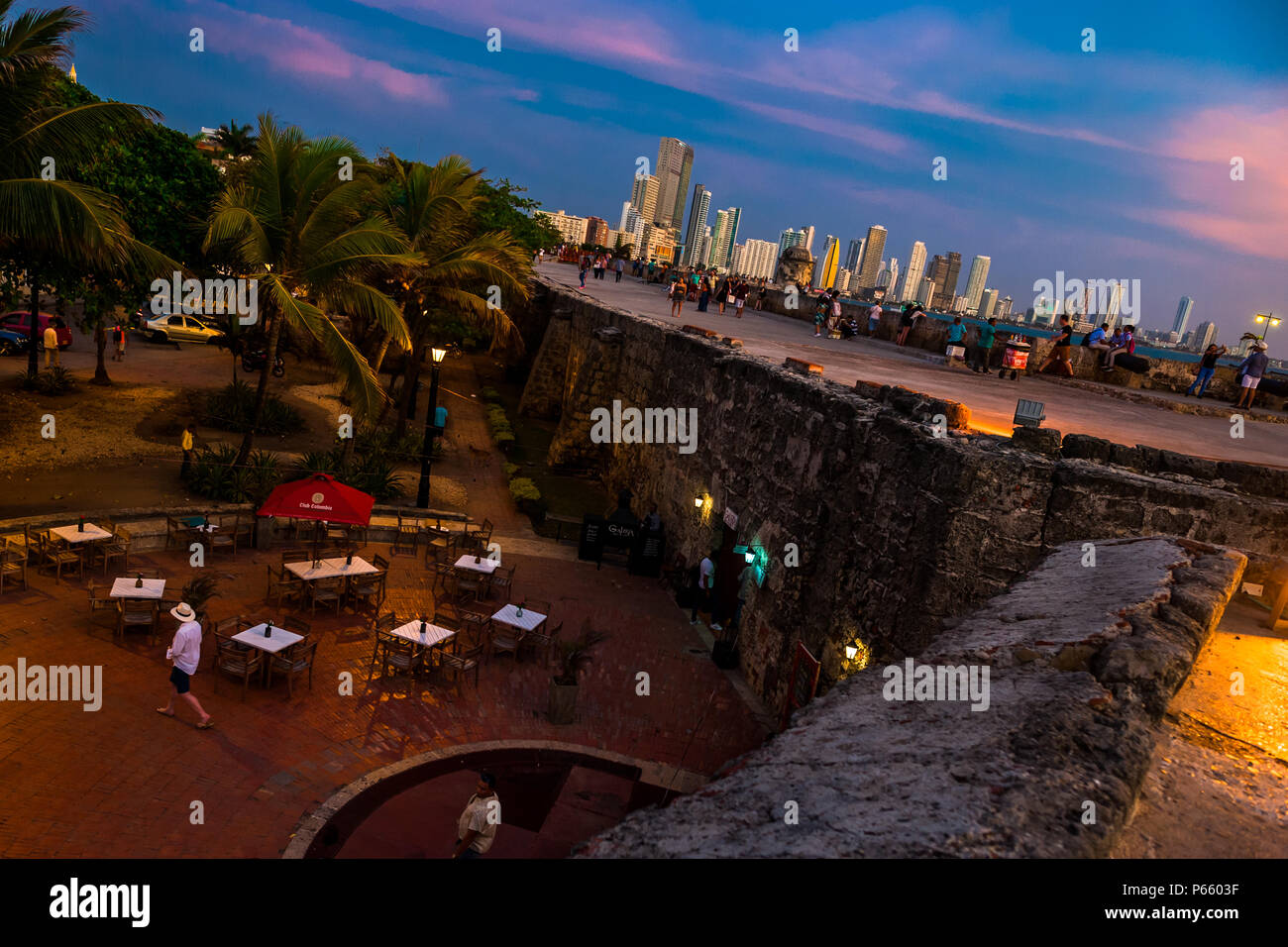 Tourists walk on and along the stone walls, surrounding the colonial walled city, at twilight in Cartagena, Colombia. Stock Photo