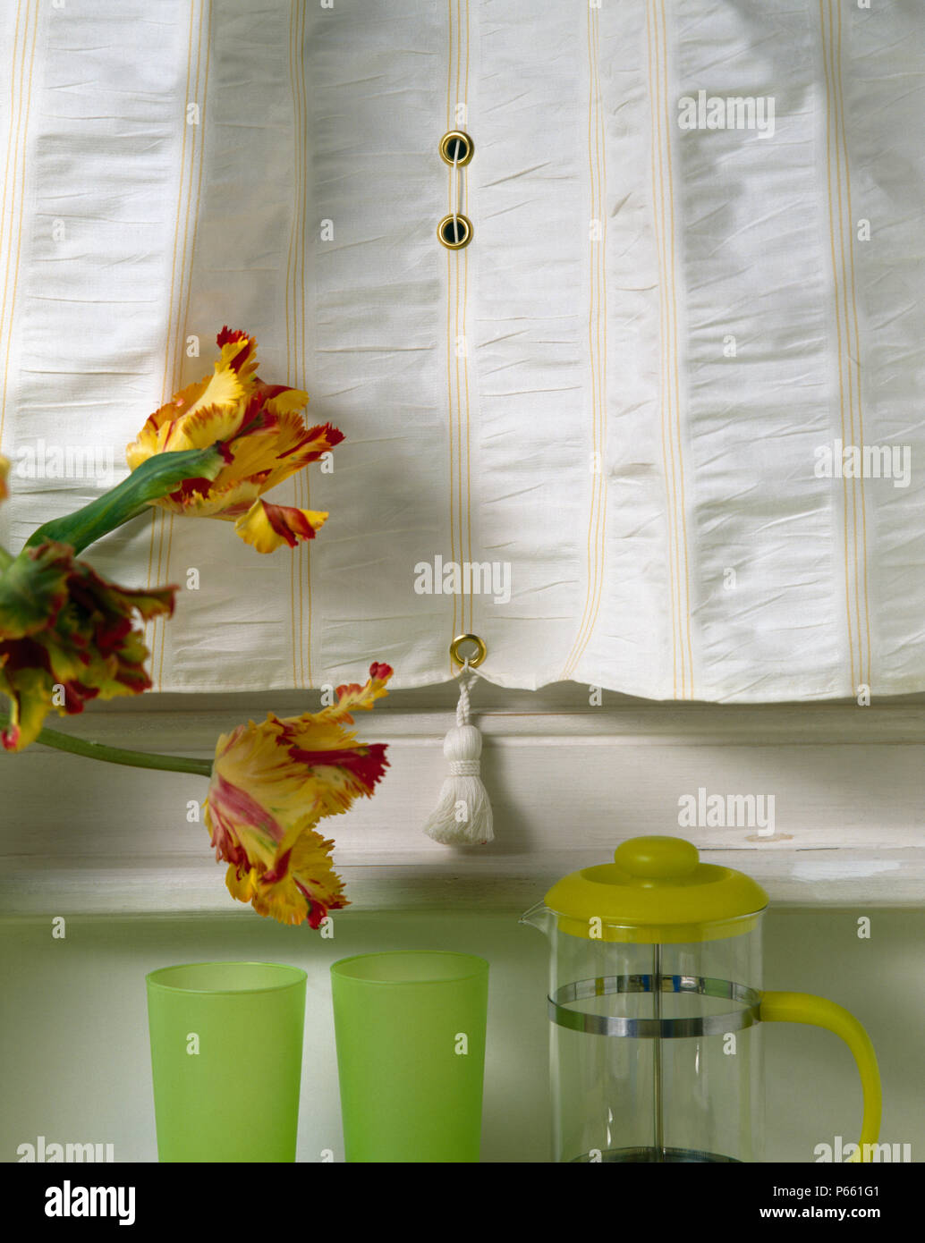 Close-up of cream ruched blind above table with yellow cafetiere and green glasses Stock Photo