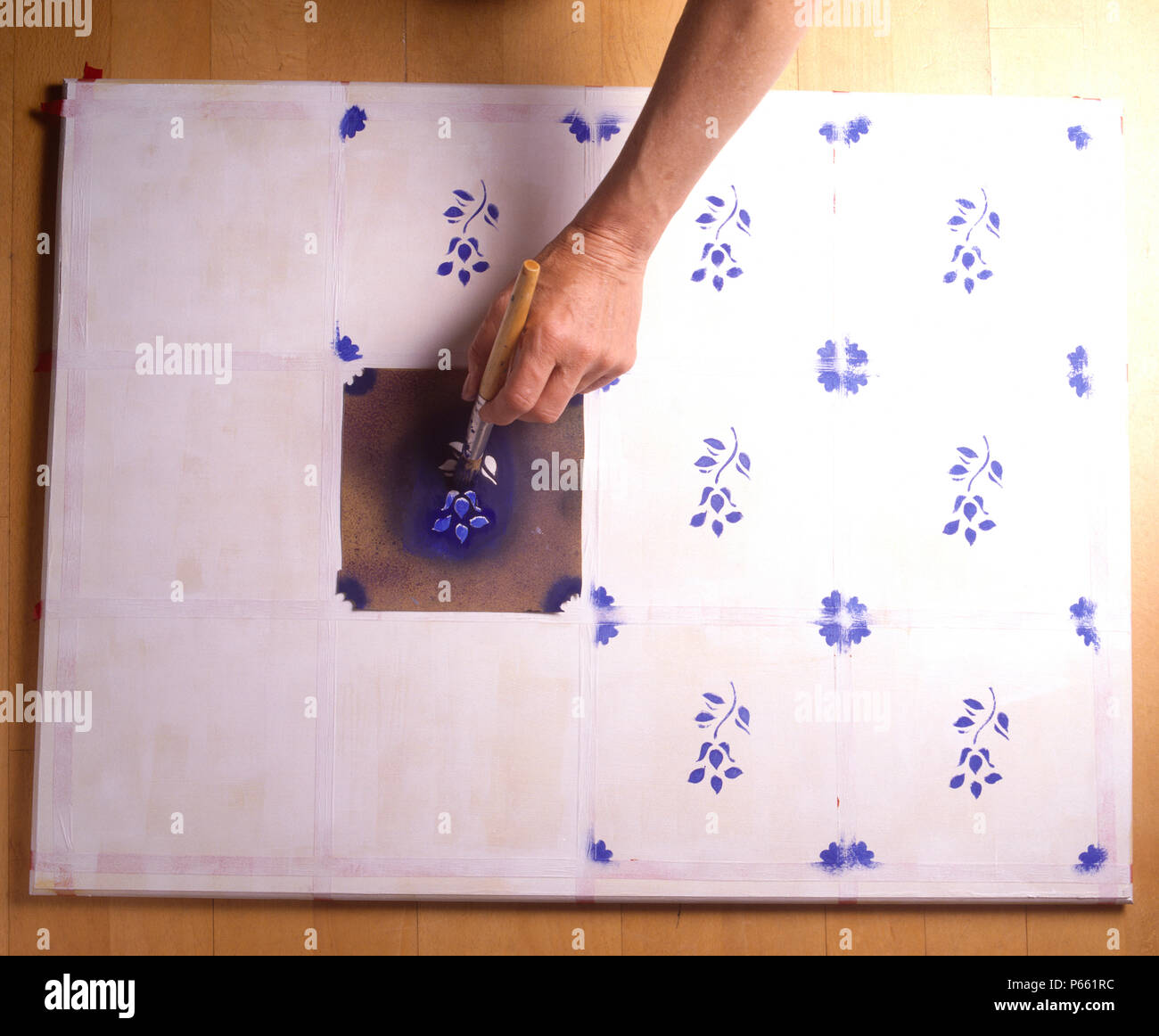 Close-up of a hand stenciling a blue floral pattern onto a marked out grid for a tile effect top for a table Stock Photo
