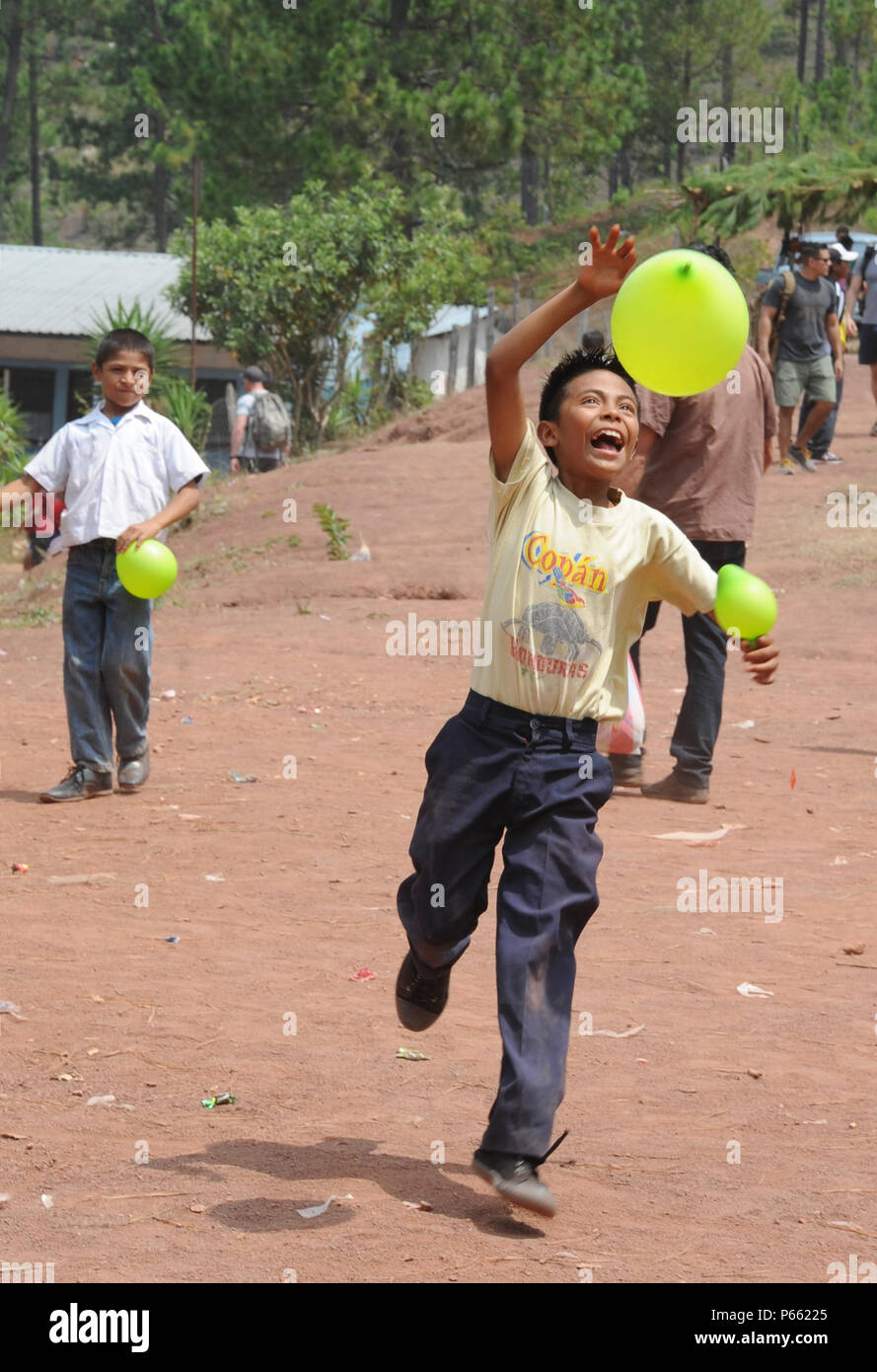 A Honduran boy from the village of Montaña La Oki, located in the mountains east of Comayagua, Honduras, plays with a balloon given to him by one of the 158 military and civilian members of Joint Task Force-Bravo and volunteer firefighters from the local area who hiked 7.4 miles roundtrip to deliver 3,000 pounds of food to 172 families in the village April 30, 2016. During the visit to Montaña La Oki, U.S. service members had the opportunity to watch local school children perform cultural dances, play soccer and hand out the bags of food to villagers as well as some Hondurans who traveled to t Stock Photo