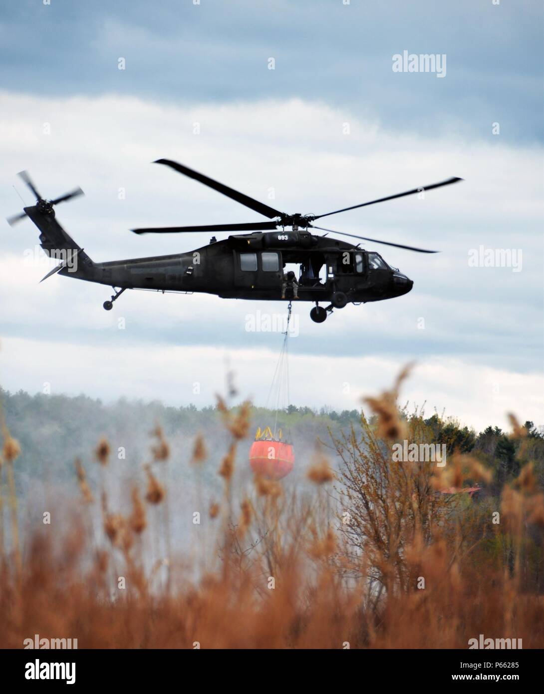 A New York Army National Guard UH-60 Blackhawk based in Latham, N.Y. hovers in place while doing swift load and drop water bucket training at Round Lake N.Y.on Thursday May 5, 2016. The National Guard conducts this training annually to practice flying with that much additional weight under the aircraft. The Soldiers are part of the 42nd Combat Aviation Brigade. (U.S. Army National Guard Photo by Capt. Jean Marie Kratzer/ Released) Stock Photo