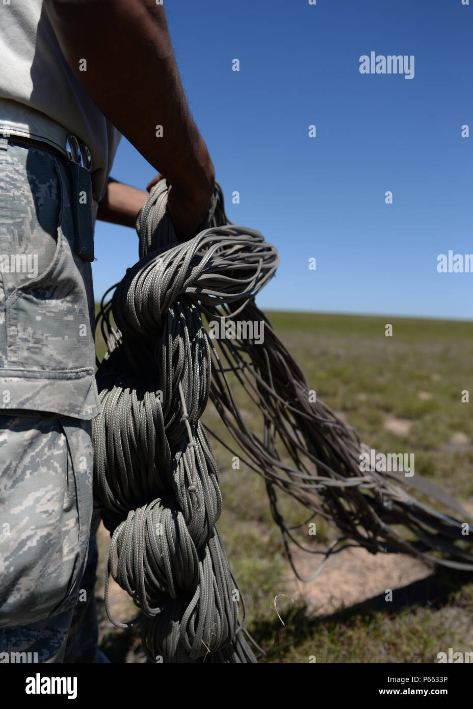 An Airman from the 97th Logistics Readiness Squadron shortens the paracord lines of a parachute after the cargo platforms were dropped from a U.S. Air Force C-17 Globemaster III cargo aircraft, May 4, 2016 Duke, Okla. Riggers build each platform used for loadmaster air drop training from the ground up, including packing the parachutes, securing the cargo, loading it into the aircraft and recovering it after it has landed. (U.S. Air Force photo by Senior Airman Nathan Clark/Released) Stock Photo