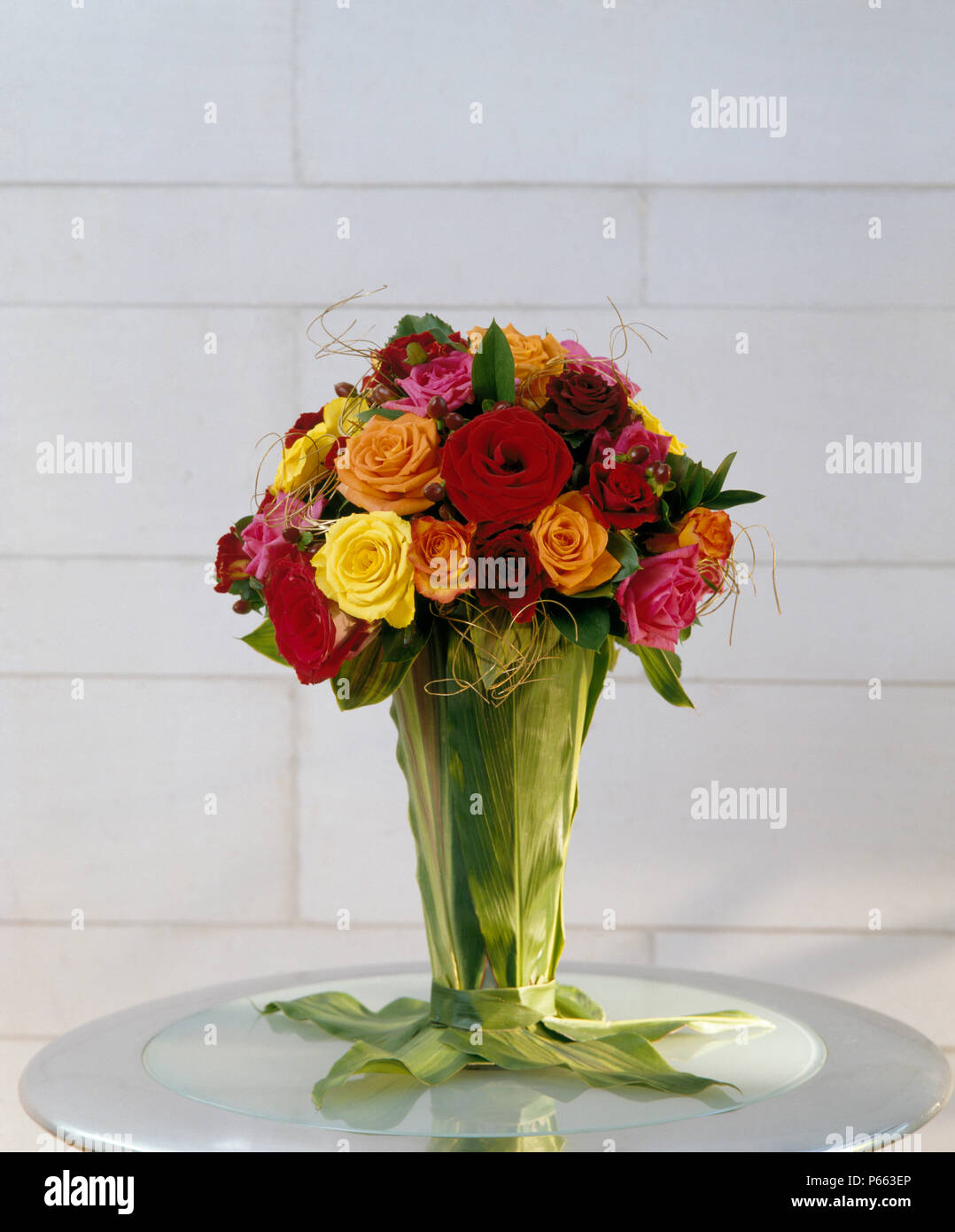 StillLife of brightly coloured roses in leaf covered vase Stock Photo