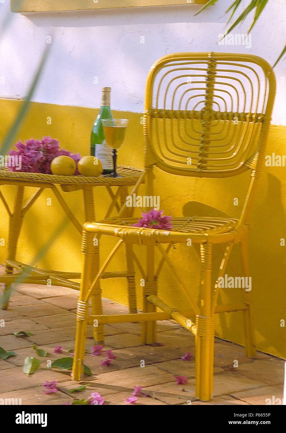 Still-Life of yellow painted cane chair and tablewith purple bougainvillea Stock Photo