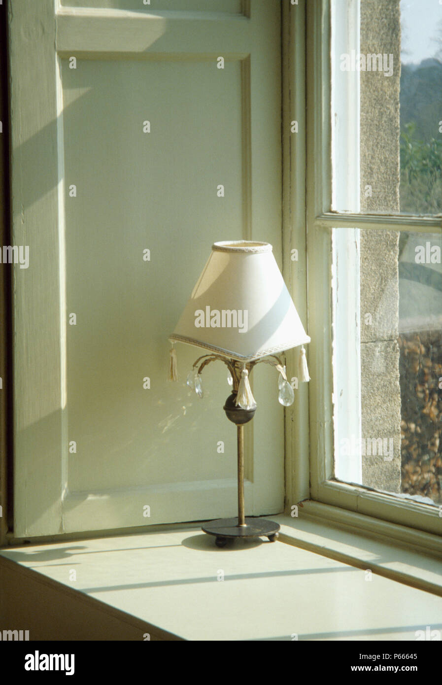 Close-up of metal lamp with white shade trimmed with glass crystals on window sill Stock Photo
