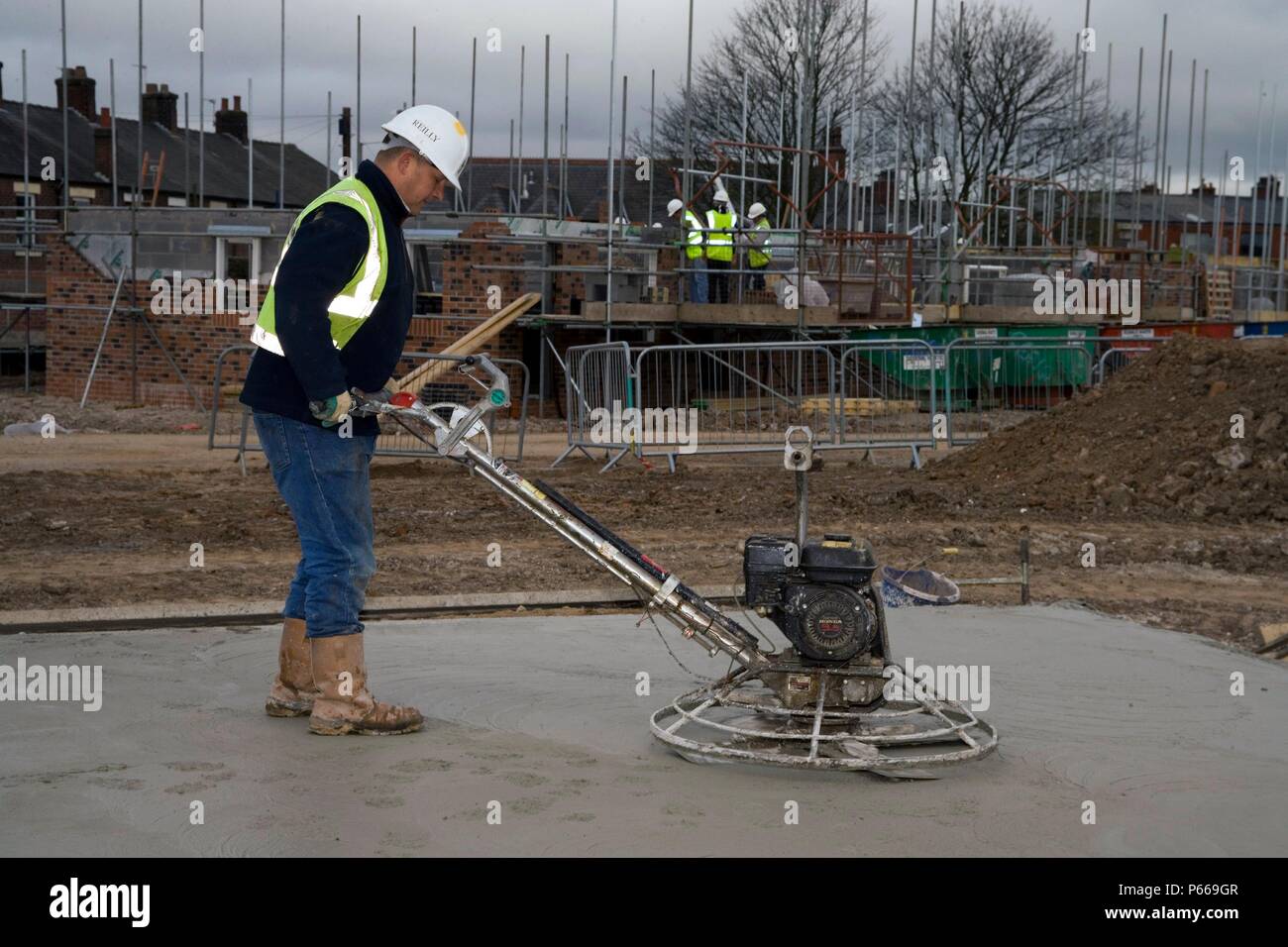 Worker in hard hat and reflective jacket using a power float to polish a concrete foundation slab. Stock Photo