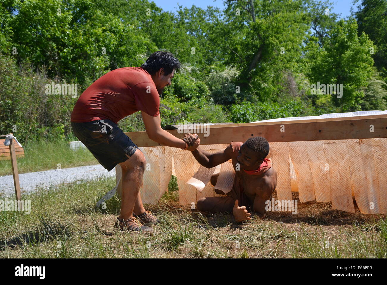 Alex Flores, of San Bernardino, Calif., pulls Chris Johnson, of Detroit, Mich., out of the 'Birth Canal' obstacle at the 2016 Atlanta Tough Mudder event. Partnered with the Army Marketing Research Group, the muddy event was held May 7 and 8, 2016, at Bouckaert Farms in Fairburn, Ga. Stock Photo