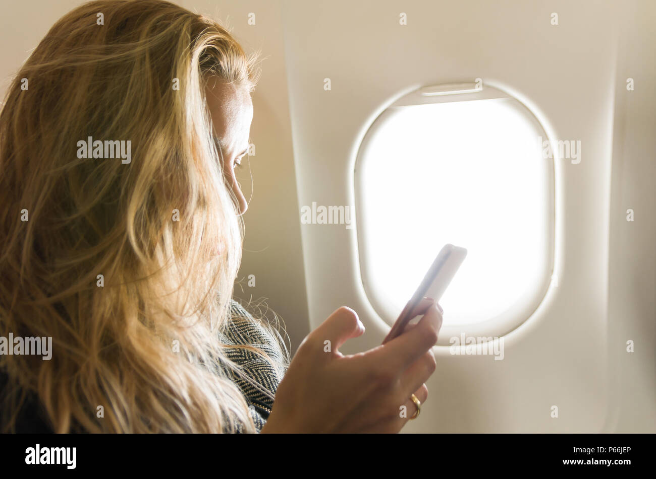 Young blond woman using smartphone on airplane Stock Photo