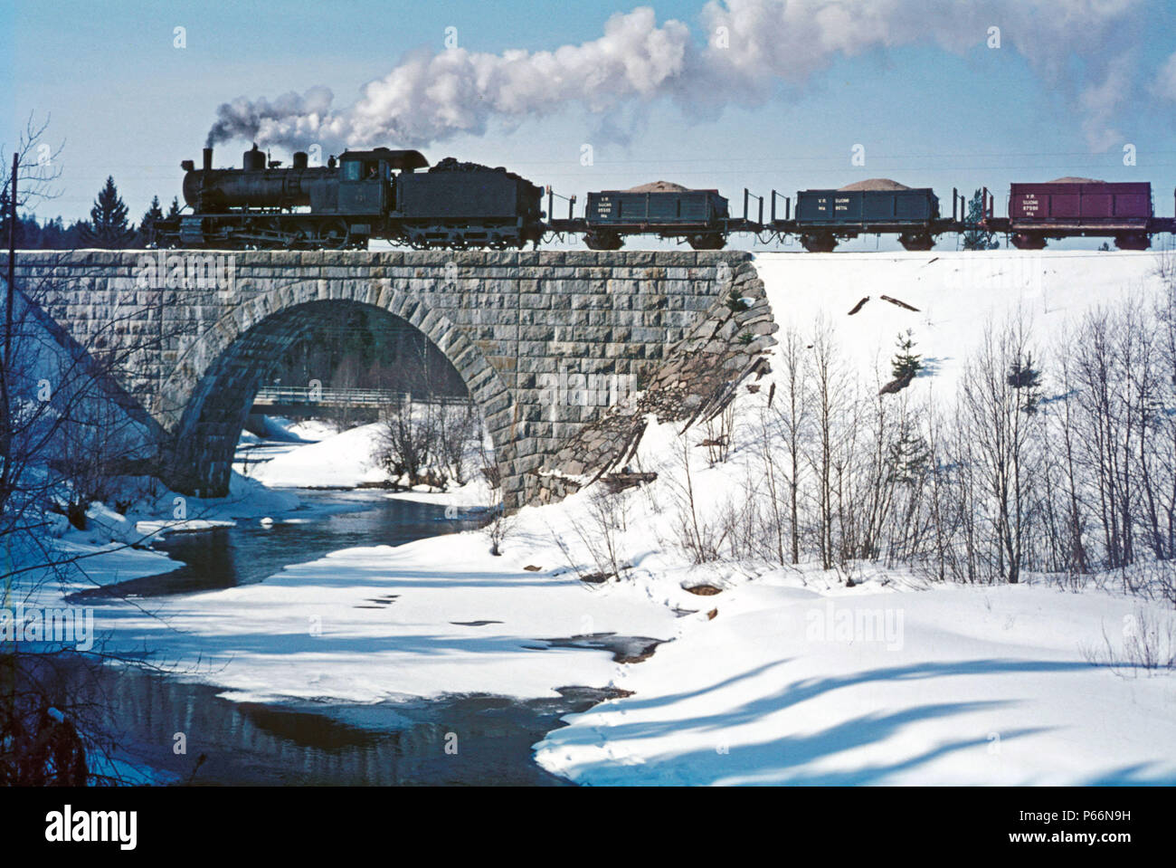 Finland's frozen rivers begin to flow again as springtime advances. Here at Hyrynsalmi, Finnish Railway's TV1 Class 2-8-0 No.921 heads a train enginee Stock Photo