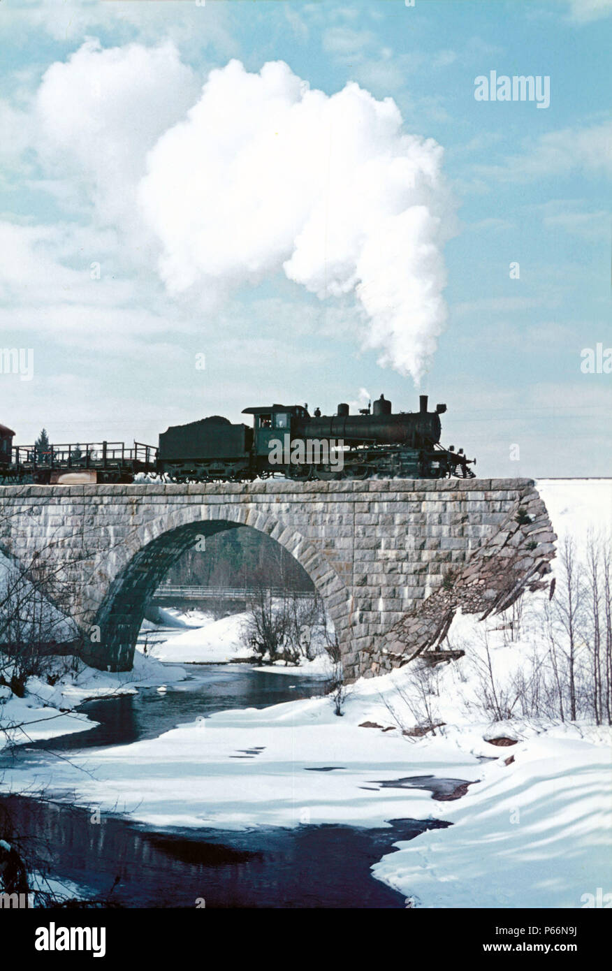 Finland's frozen rivers begin to flow again as springtime advances. Here at Hyrynsalmi, Finnish Railway's TV1 Class 2-8-0 No.921 heads a train enginee Stock Photo