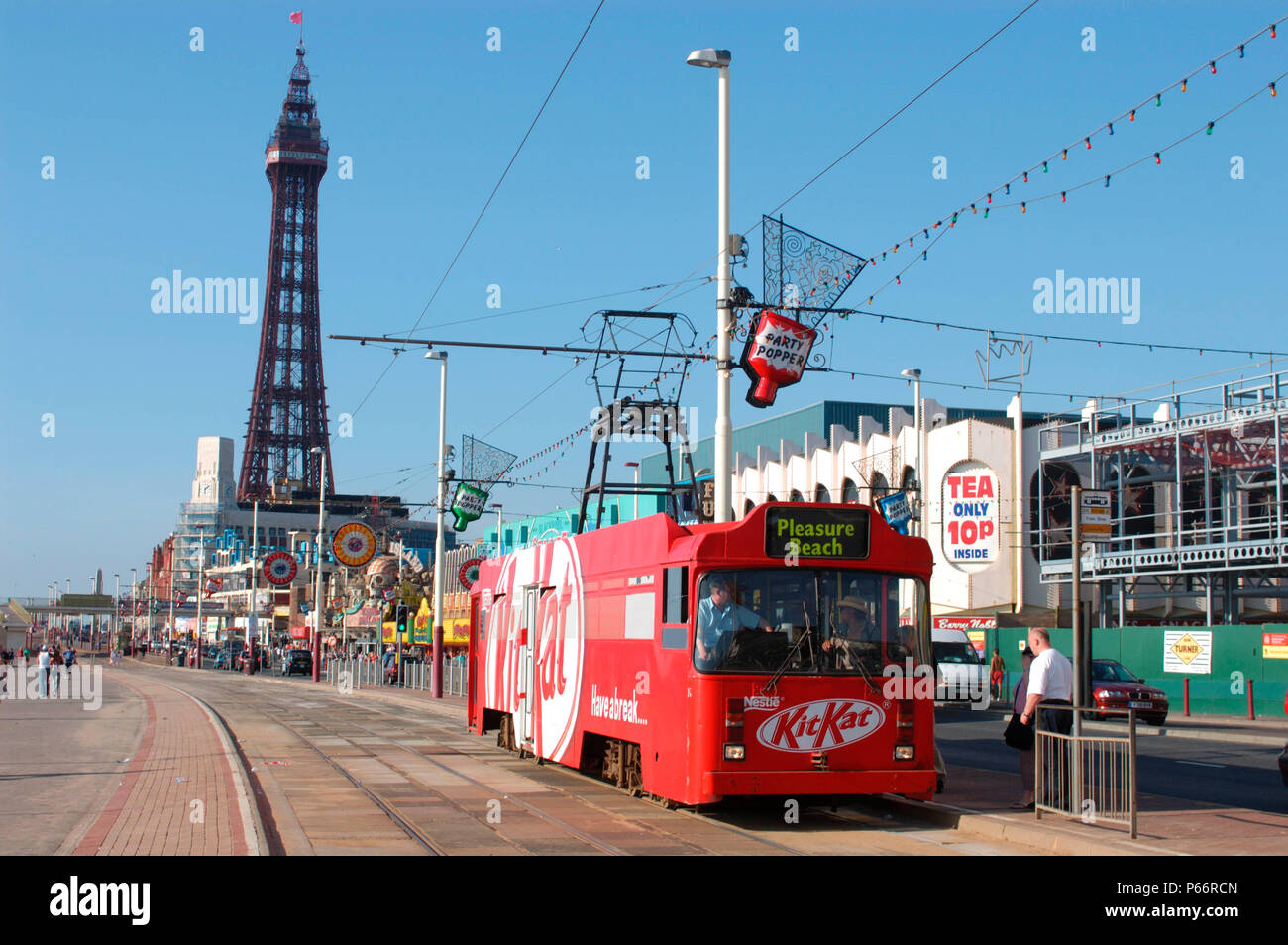 One of Blackpool's famous heritage trams, complete with advertising for a chocolate confectionary, traverses the promenade with Blackpool Tower in the Stock Photo