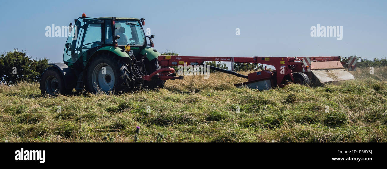 A farm tractor pulling Kuhn grass cutting mcahinery in a field in Northern Irelan Stock Photo