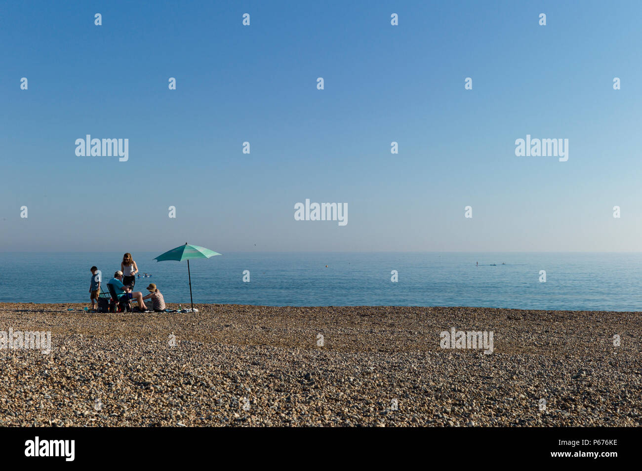 Family picnic under umbrella on empty beach, Seaford, Sussex Stock Photo