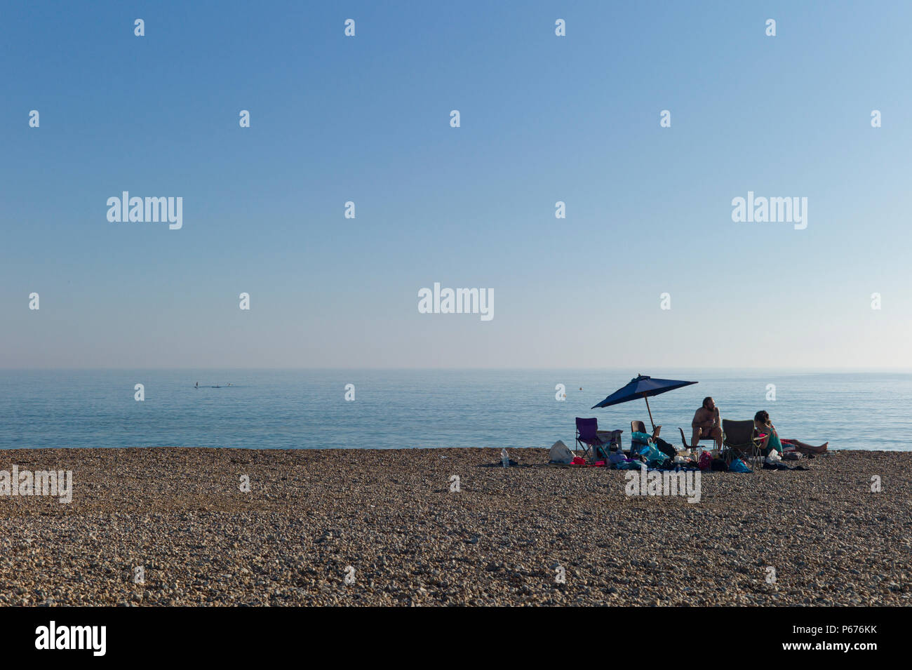 Family picnic under umbrella on empty beach, Seaford, Sussex Stock Photo