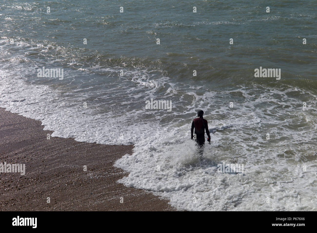 Man in wetsuit preparing to swim in rough water, Brighton, UK Stock Photo
