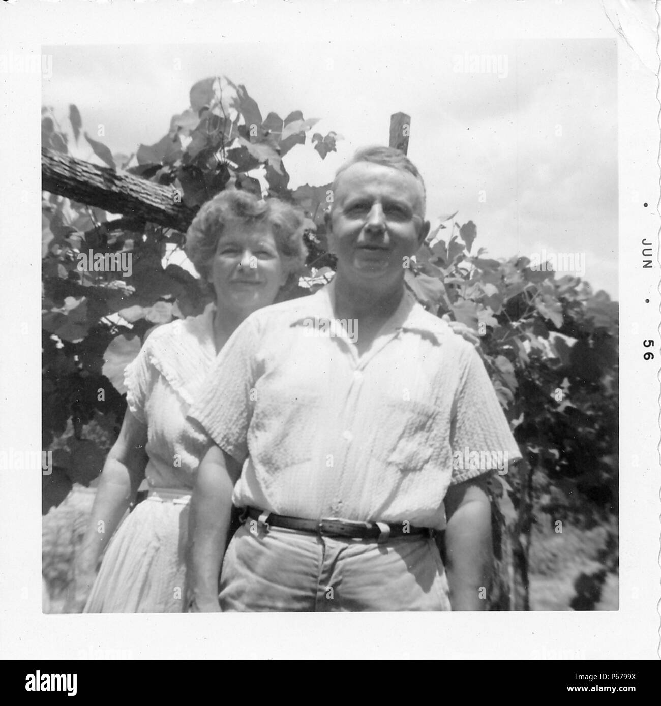 Black and white photograph, showing a man standing in front of a woman, both in their forties, from the waist up, standing outside, facing the camera, with foliage visible in the background, photographed in Ohio, 1956. () Stock Photo