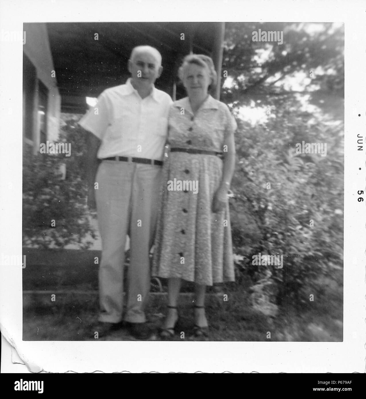 Black and white photograph, showing a man and a woman in their sixties, standing in full length, outside, facing the camera, with their arms around each other's back, and serious expressions on their faces, with foliage and part of a house visible in the background, likely photographed in Ohio, 1955. () Stock Photo