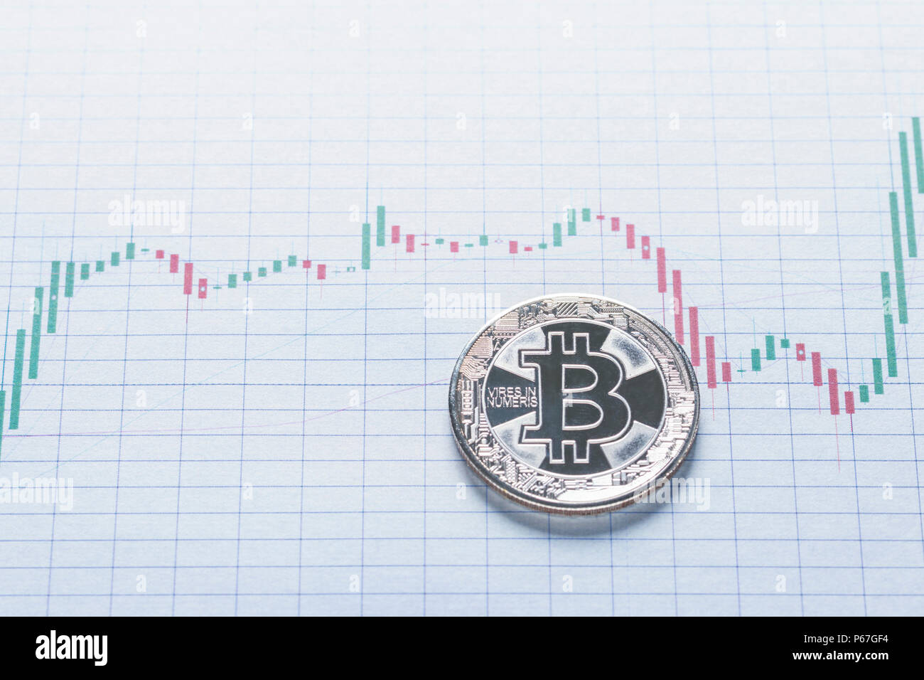 Bitcoin price volatility concept presented as single silver coin laid on increasing and decreasing in value chart candles Stock Photo