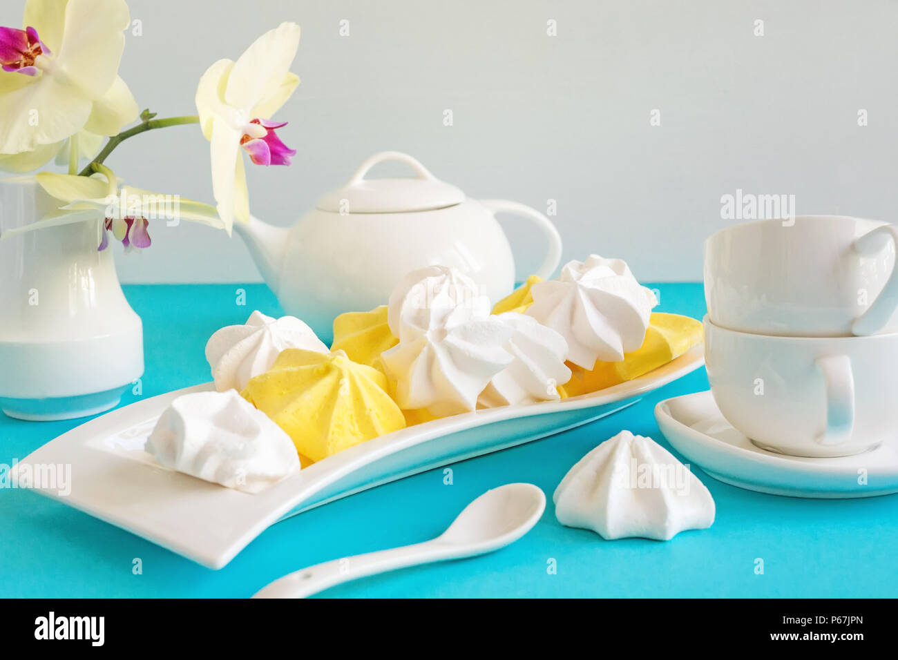 White and yellow meringue on blue background in tea serving with white kettle. Stock Photo