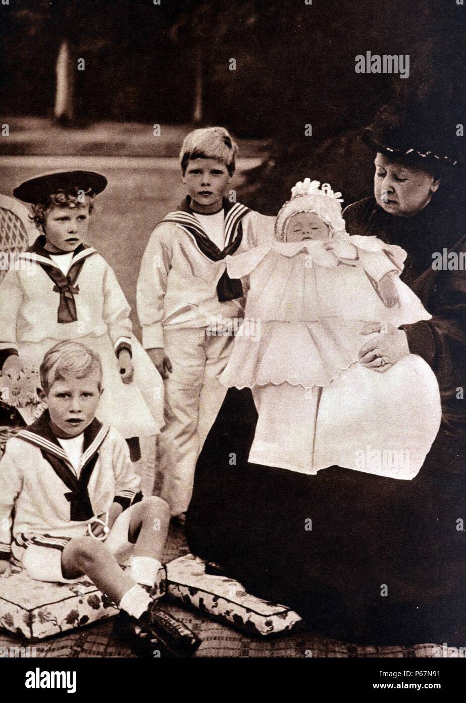 Royal Family portrait shows Queen Victoria with her 4 grandchildren. Princess Mary is shown wearing a hat, to her right is Prince Edward, Prince Albert is seated at the front and the newborn, Prince Henry is in Victoria's arms. Stock Photo