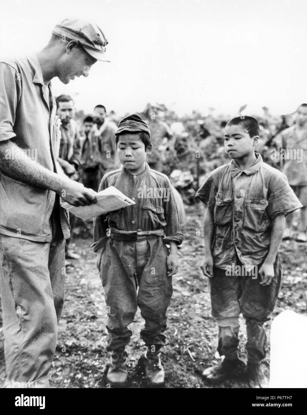 Photograph of an American Marine trying to communicate with two Japanese child soldiers captured in Okinawa. Dated 1945 Stock Photo