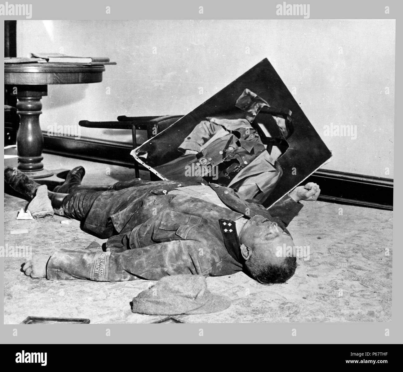 Photograph of the body of Walter Doenicke, battalion leader of a German national militia, lies next to a torn portrait of Hitler. In Leipzig. Dated 1945 Stock Photo