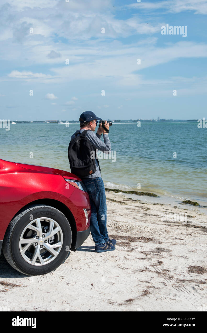 man leaning on a car taking photographs of the Gulf of Mexico with a DSLR camera Stock Photo