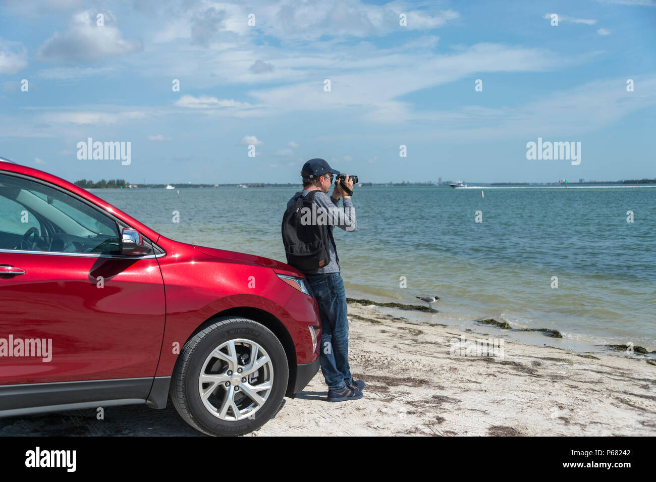 man leaning on a car taking photographs of the Gulf of Mexico with a DSLR camera Stock Photo