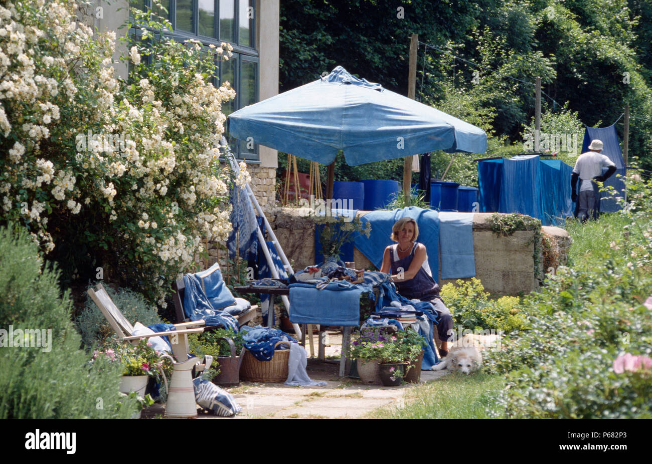 Woman sitting below blue umbrella in garden with fabric and clothes dyed with blue indigo dye         FOR EDITORIAL USE ONLY Stock Photo