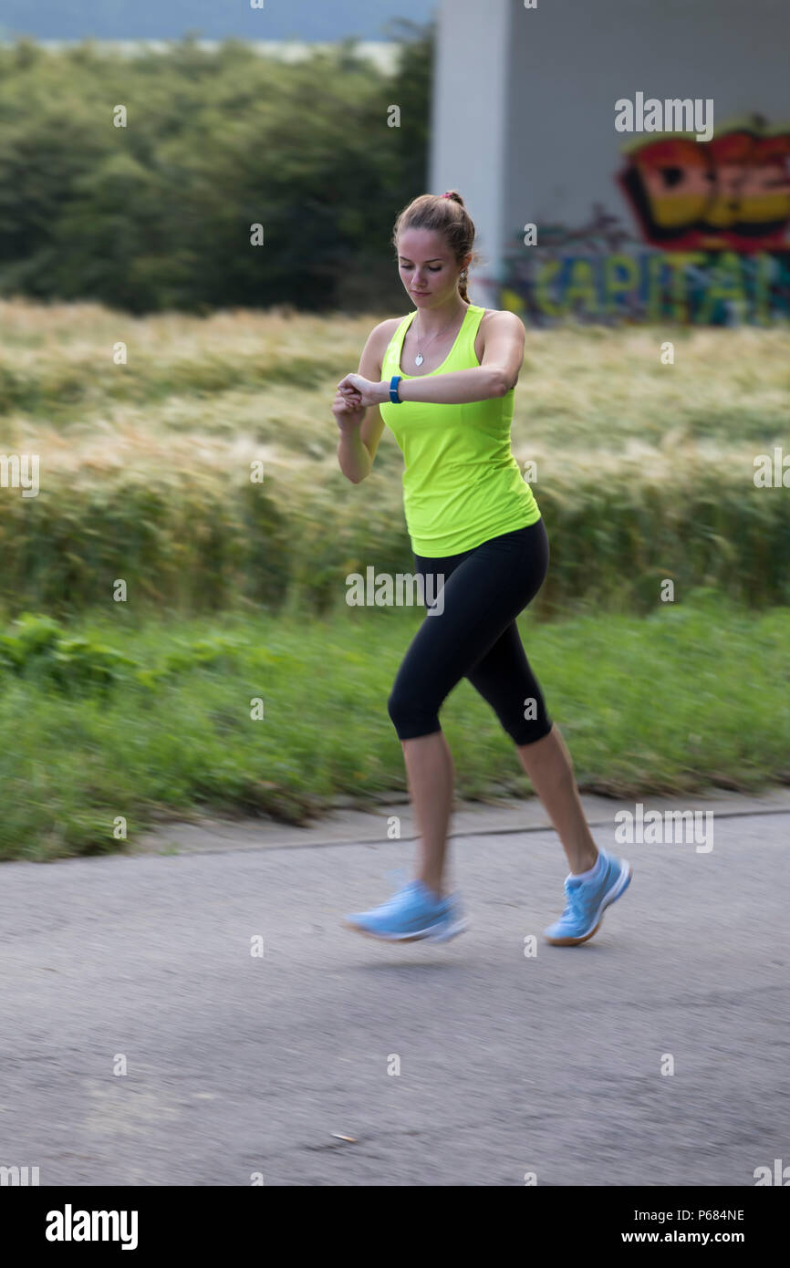 Young woman jogging, running, checking her vital signs on a fitness watch, fitness tracker, heart rate, number of steps, distance, time, calories burn Stock Photo