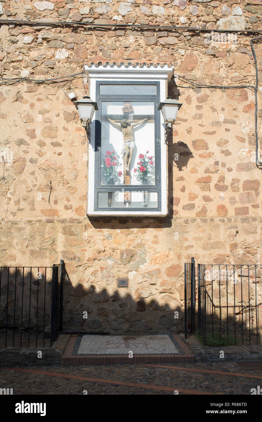 Christian crucifix stands encased and attached outdoors to wall of Church of Sta. Mª. de las Cruces, Saceruela, Ciudad Real, Spain Stock Photo