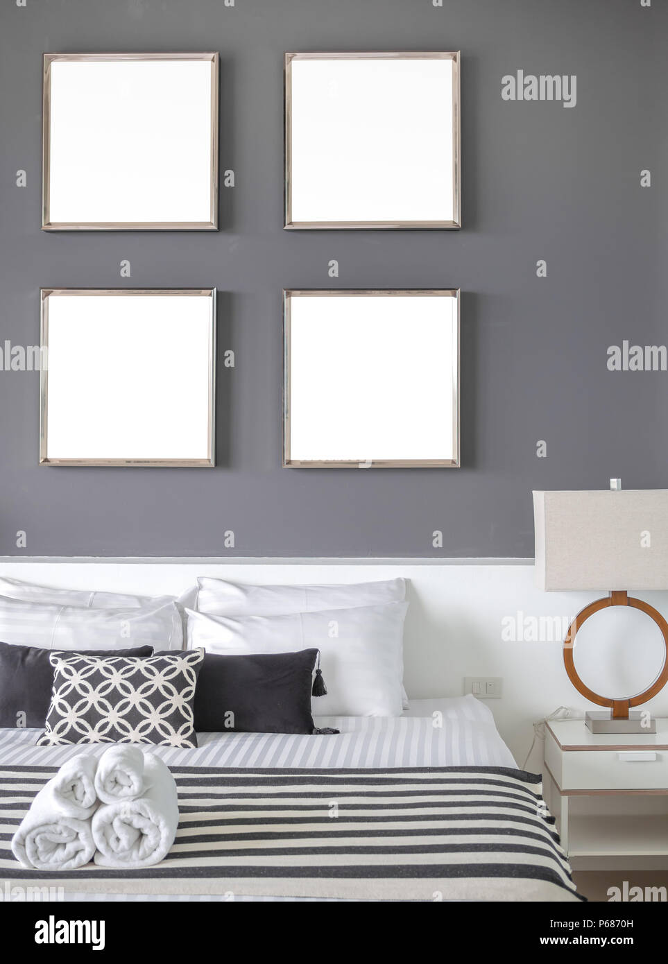 Modern Bedroom with Four Square Blank Stainless Steel Frames on The Gray Wall Interior, Pillows and Towels on The Bed with Side Lamp. Stock Photo
