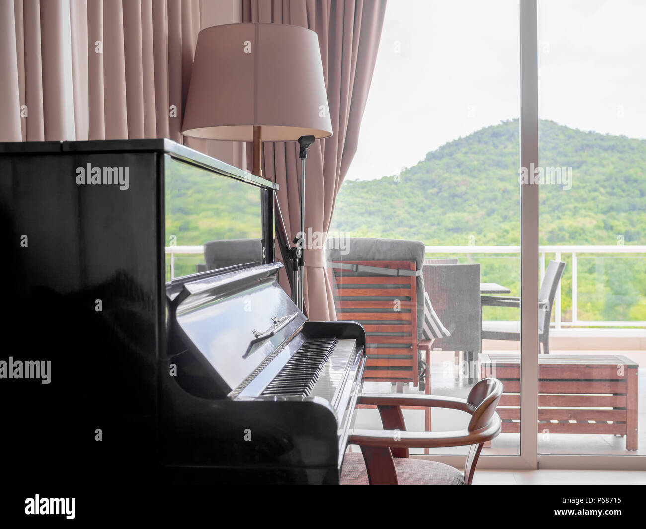 Classic Piano in Living Room with Chair and Floor Lamp Near The Sliding Door to The Terrace Outside with Mountain View. Stock Photo