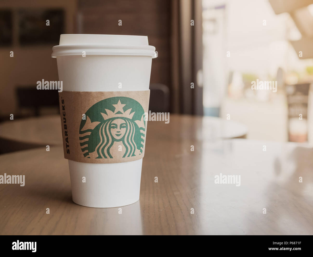 Samut Songkhram, THAILAND - June 21, 2018: Hot Coffee in White Plastic Take Away Coffee Cup on Wooden Table Beside The Glass Window in The Starbucks C Stock Photo