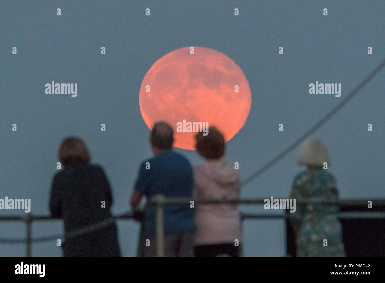 Mousehole, Cornwall, UK. 28th June 2018. UK Weather. A group of friends stand on the harbour wall at Mousehole, watching the full Strawberry moon rise. Credit: cwallpix/Alamy Live News Stock Photo