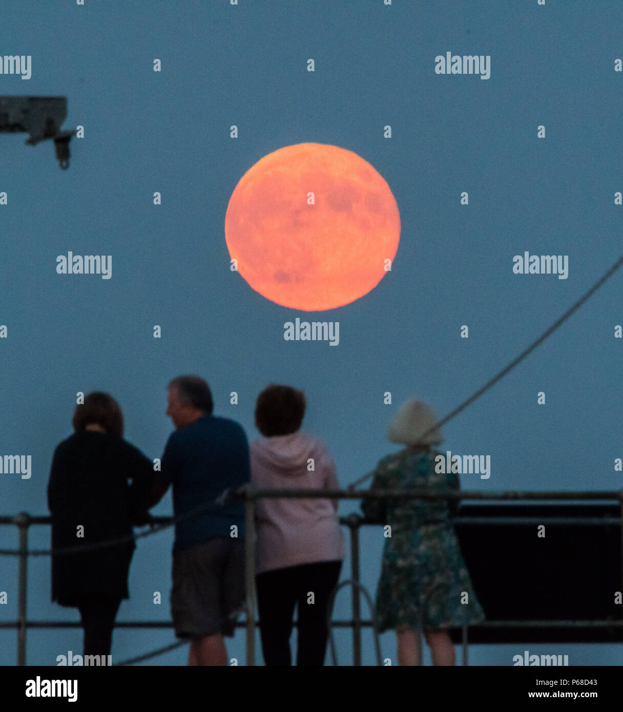 Mousehole, Cornwall, UK. 28th June 2018. UK Weather. A group of friends stand on the harbour wall at Mousehole, watching the full Strawberry moon rise. Credit: cwallpix/Alamy Live News Stock Photo