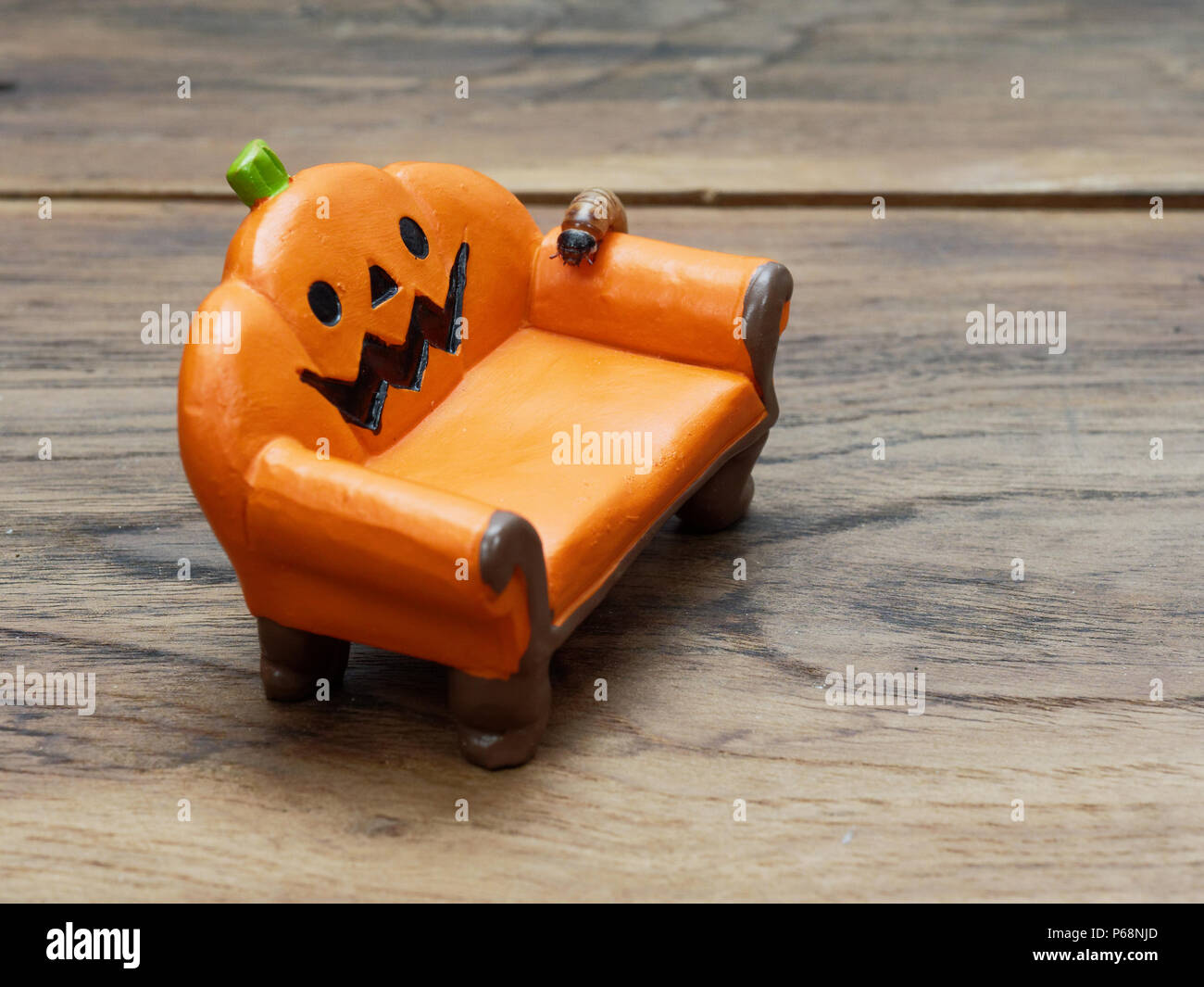 Super or giant worm crawling on orange miniature ceramic pumpkin couch or sofa over dark wooden surface with copy space used as background in Halloween, ornament, celebration, and decoration Stock Photo