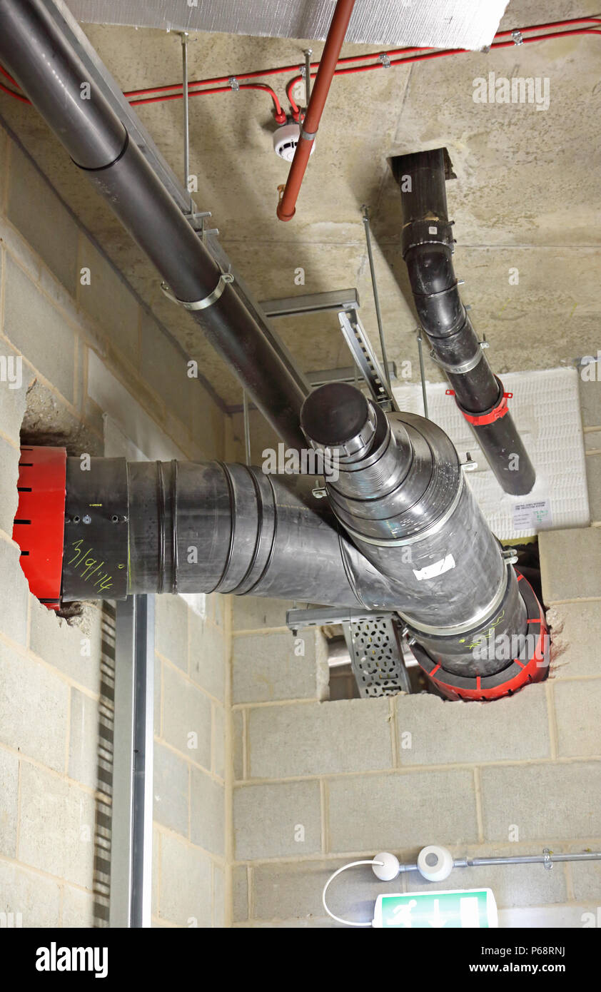 Plastic soil and waste drainage pipes in basement of a new London tower block. Shows firetrap collars to maintain fire integrity through wall openings Stock Photo