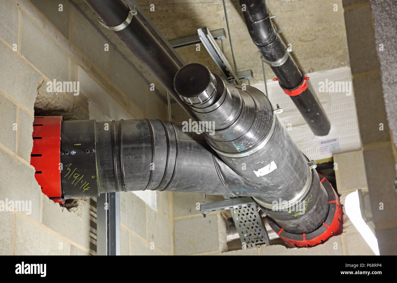 Plastic soil and waste drainage pipes in basement of a new London tower block. Shows firetrap collars to maintain fire integrity through wall openings Stock Photo