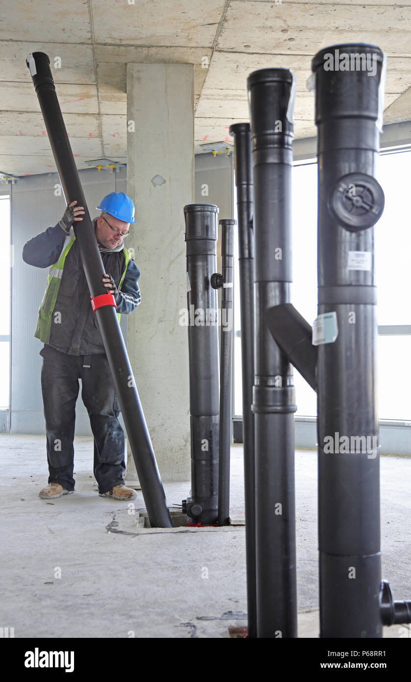 A workman installs plastic soil and waste drainage pipes in a new