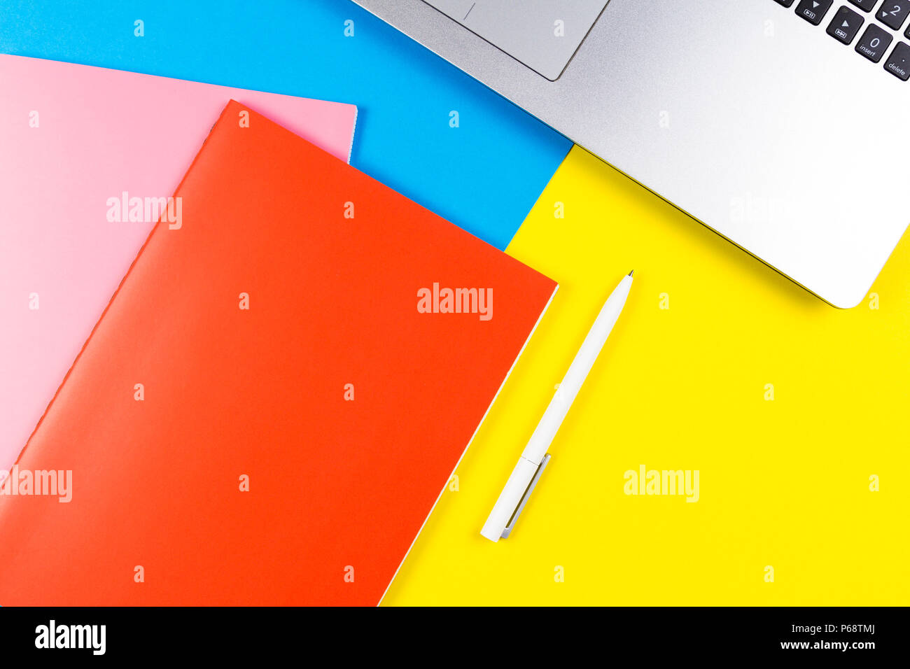 Top view of laptop computer, paper notebooks and white pen on blue and yellow color background