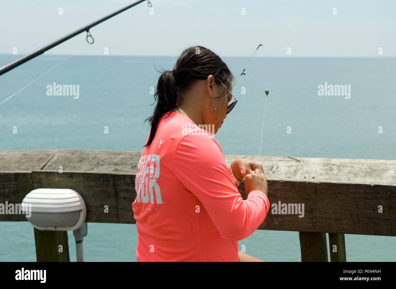 Woman baits hook for fishing on pier at Myrtle Beach State Park, SC, USA. Stock Photo